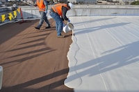 Commercial roof surface prepared with white coating and buckets of adhesive during deck installation.